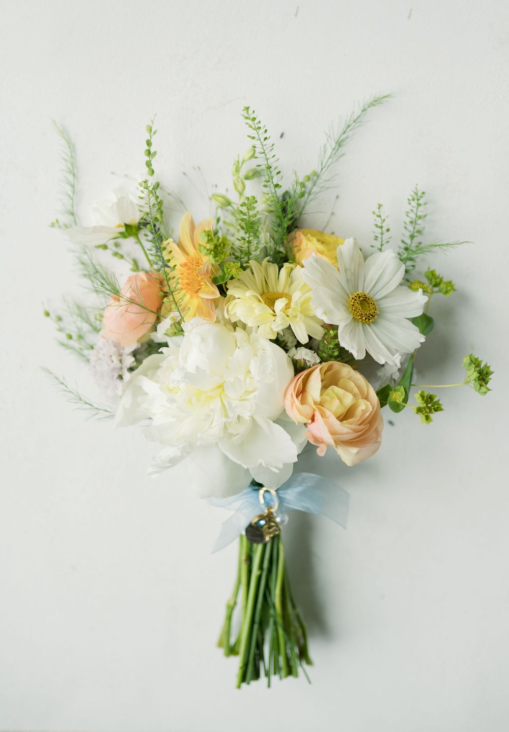 Romantic spring wedding bouquet with white, yellow and peach flowers tied with blue ribbon.