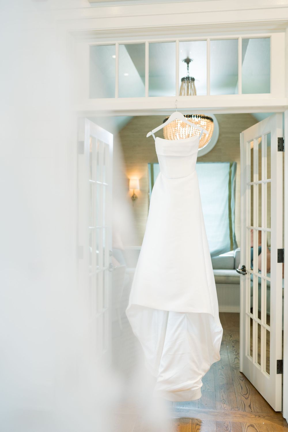 White wedding dress hanging in bright, airy room with French doors.