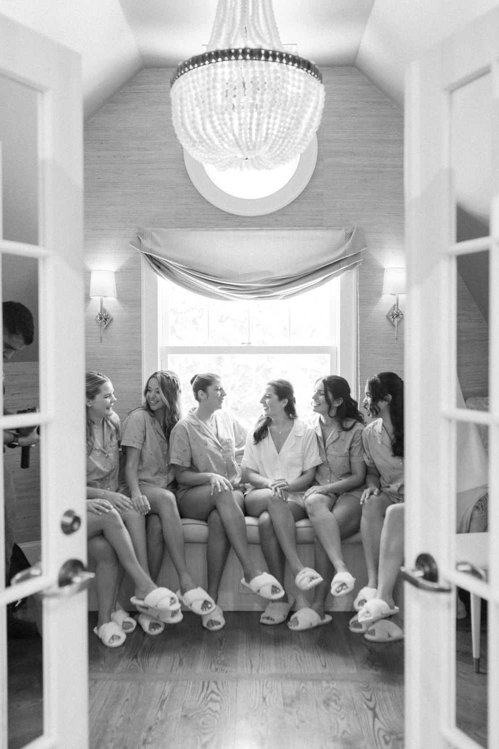 Wedding party in matching blue robes and slippers gathered under crystal chandelier in bridal suite.