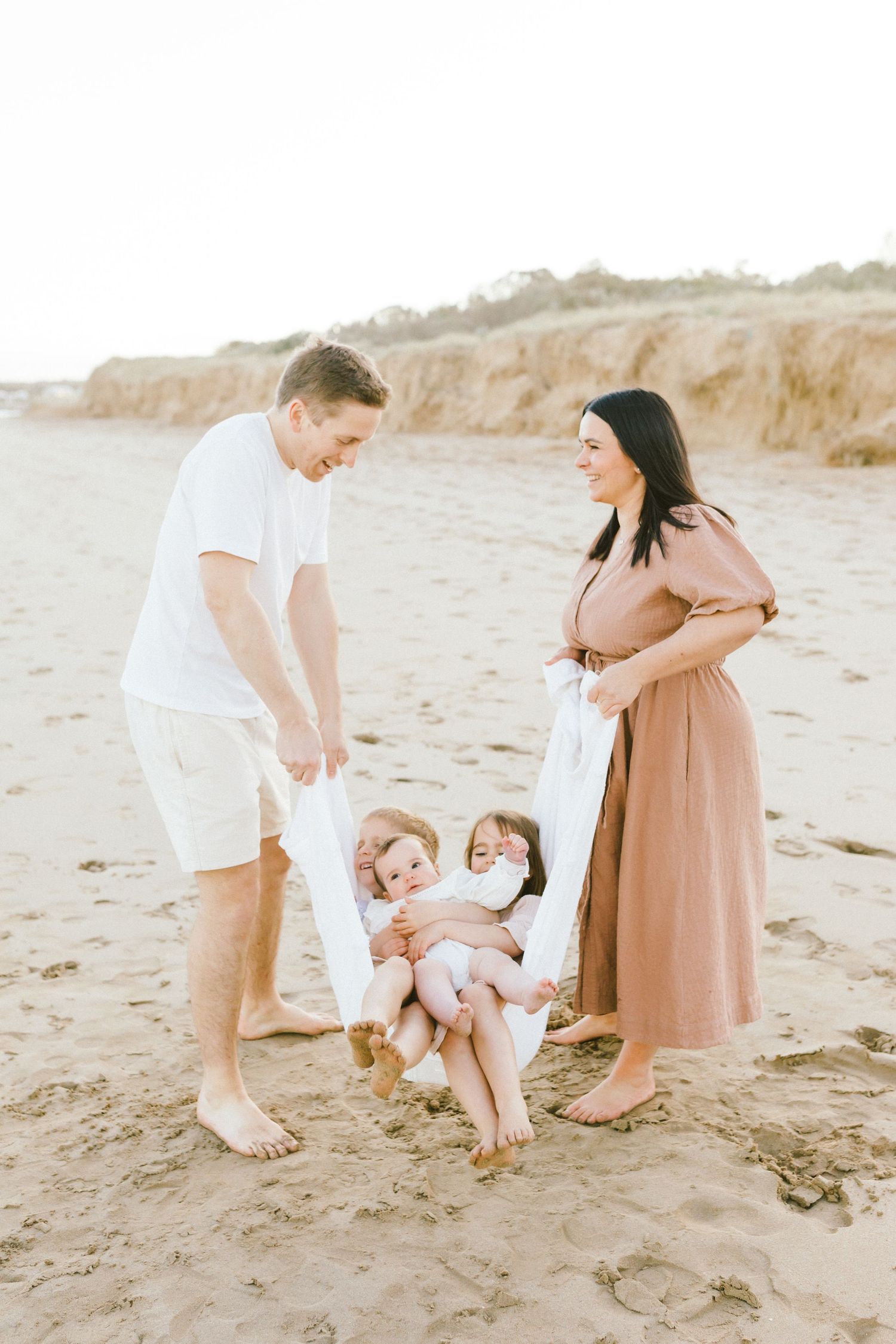 A family plays together on a sandy beach at sunset in matching white and tan outfits.