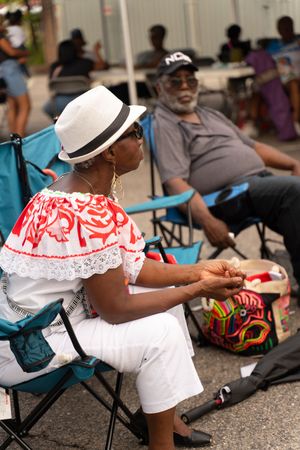 People relaxing in folding chairs wearing traditional white and red clothing at an outdoor event.
