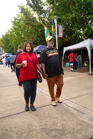 People walking through an outdoor festival with tents and flags visible in the background.