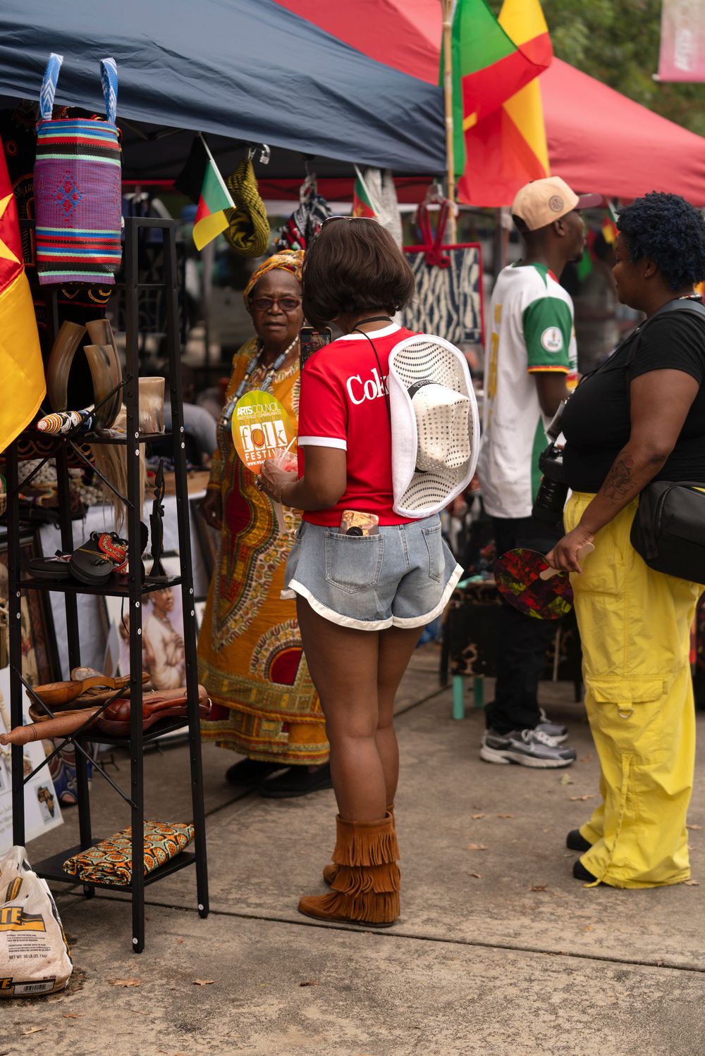 Vendors and attendees gather under tents at a cultural festival with colorful flags.