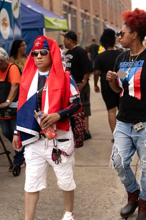 People in casual clothing and red vests walk along a brick-paved street at an outdoor event.