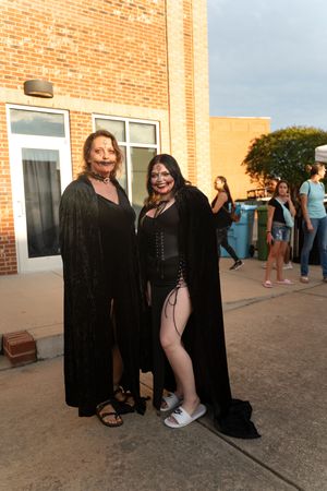 People in black outfits posing playfully against a brick building.