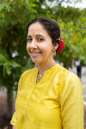 Woman in bright yellow traditional Indian attire with red flower in hair at outdoor event.
