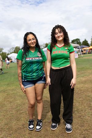 Friends in matching green shirts pose together on a grassy field at an outdoor event.
