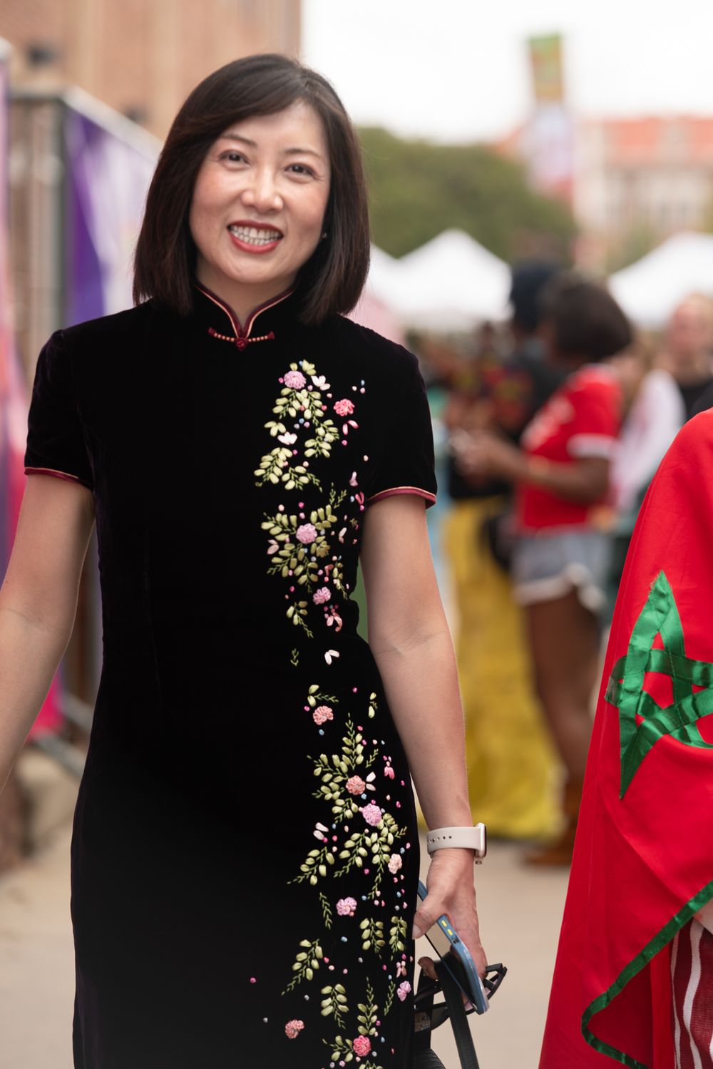 A person wearing a black traditional Chinese dress with delicate floral embroidery at an outdoor event.