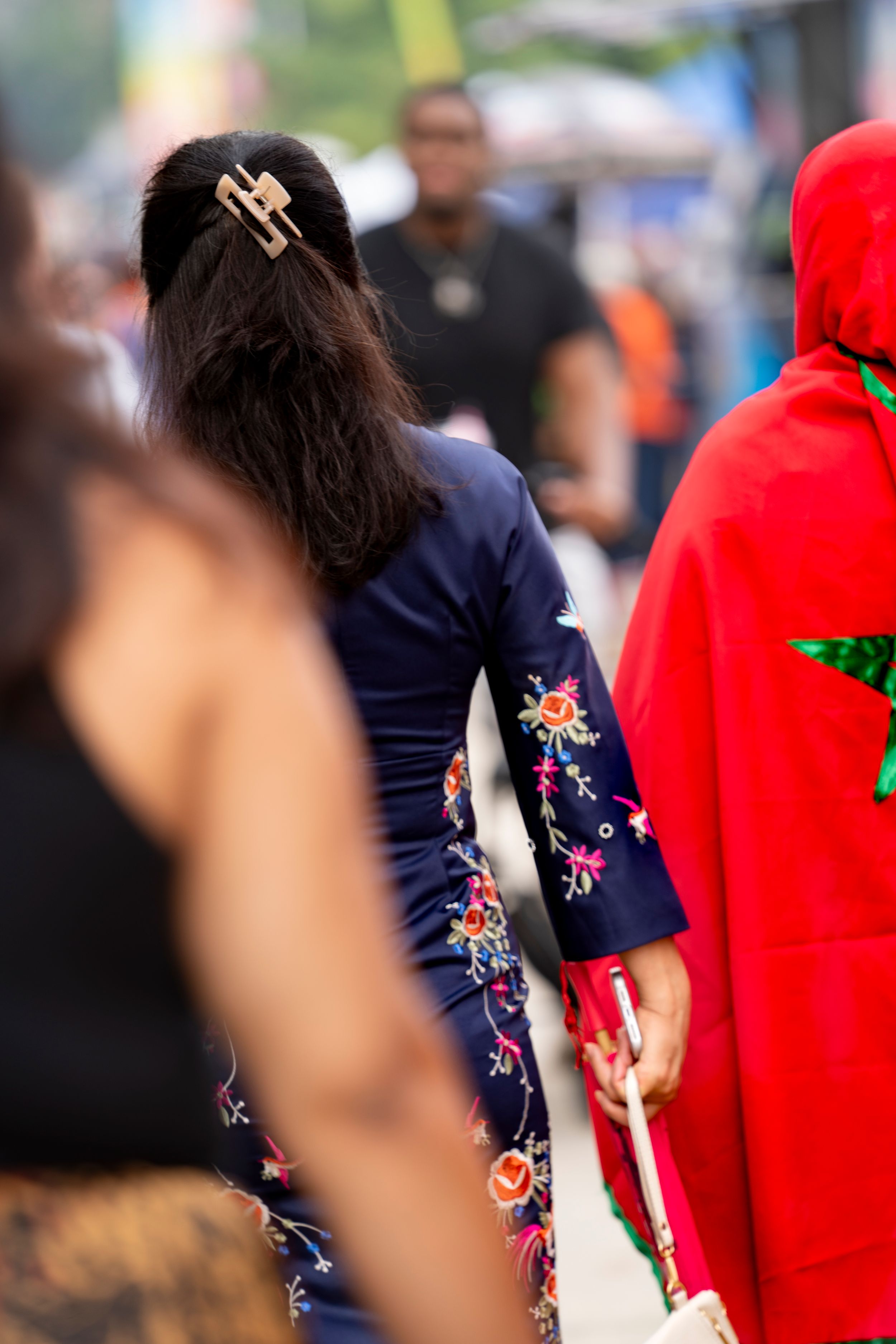 Blurred crowd scene showing colorful outfits with floral patterns and red clothing.