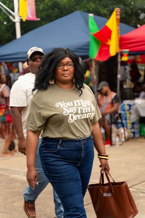 Festival attendee in casual attire carrying brown leather bag at outdoor cultural event.