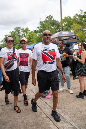 People wearing Trinidad and Tobago themed shirts walking through a festival marketplace.