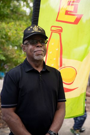 Person wearing black polo shirt and cap stands in front of bright yellow festival banner outdoors.