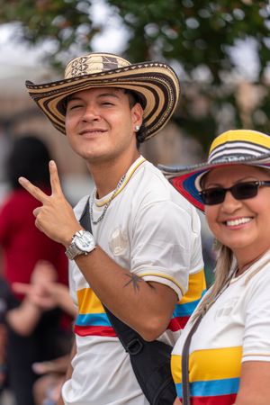 A person wearing a white shirt and straw hat gestures with their hand during an outdoor celebration.
