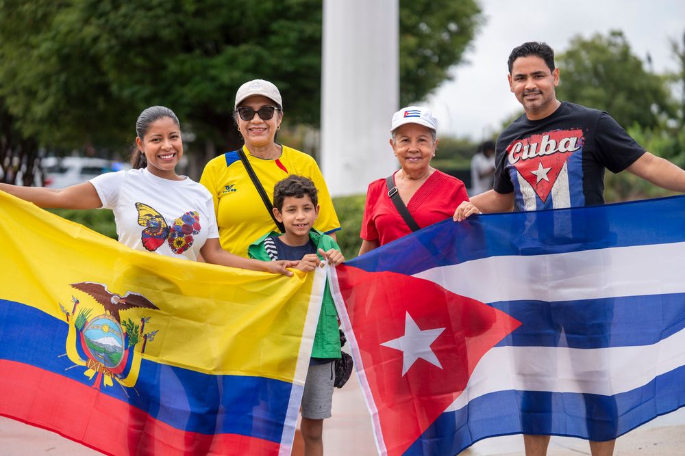 A group of people holding various national flags including Venezuela and Cuba at an outdoor gathering.