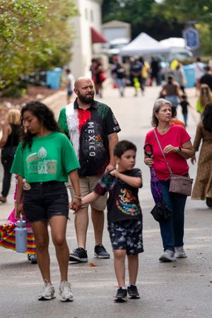 Festival attendees walking along a path outdoors with tents and vendor booths visible in the background.