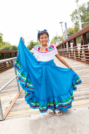 A bright blue traditional Mexican dress with colorful trim is displayed on a wooden boardwalk.