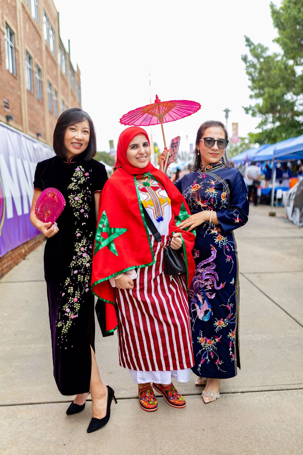 Group wearing colorful traditional Asian clothing and holding parasols poses at a cultural event.
