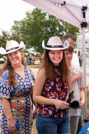 People wearing white cowboy hats and patterned shirts smiling under a white tent.