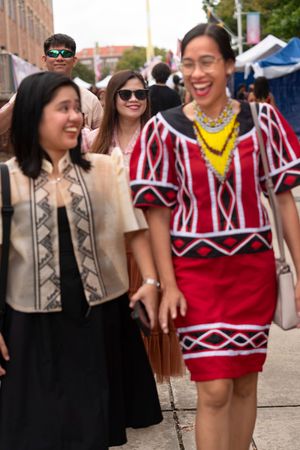 People wearing traditional red and beige cultural outfits gather at an outdoor event.