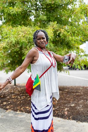 Festival attendee in white dress with red accessories poses with camera outdoors.