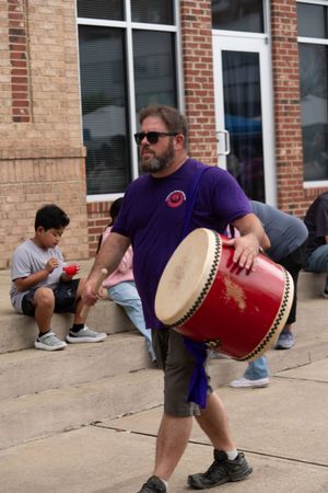 Person playing a large red drum outside a brick building.