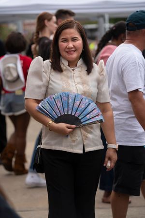 A person in traditional Filipino dress holds a decorative blue folding fan at an outdoor event.