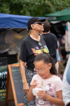 A person wearing a black t-shirt and sunglasses walks through an outdoor market area.