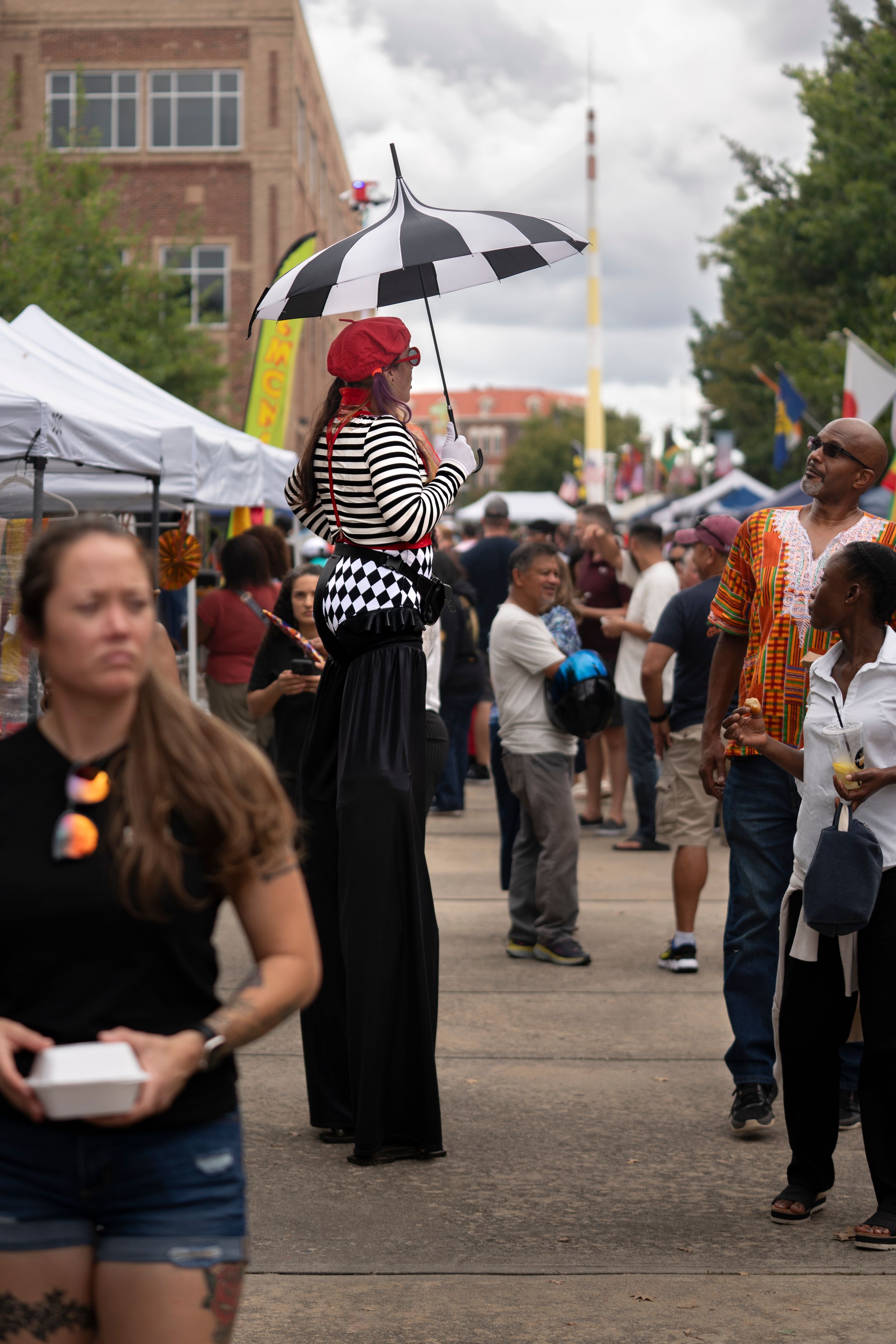 People browse vendor booths and tents at a crowded outdoor festival under cloudy skies.