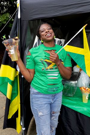 A vendor in green shirt serves drinks at a booth decorated with Jamaican flags.