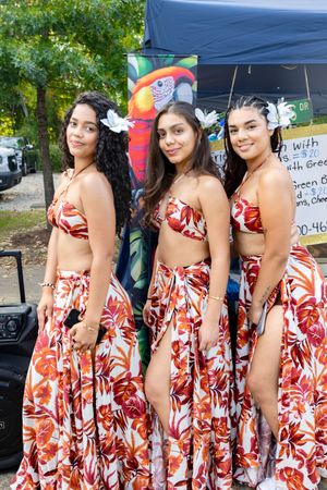 Dancers in matching red and white floral dresses posing at an outdoor event.
