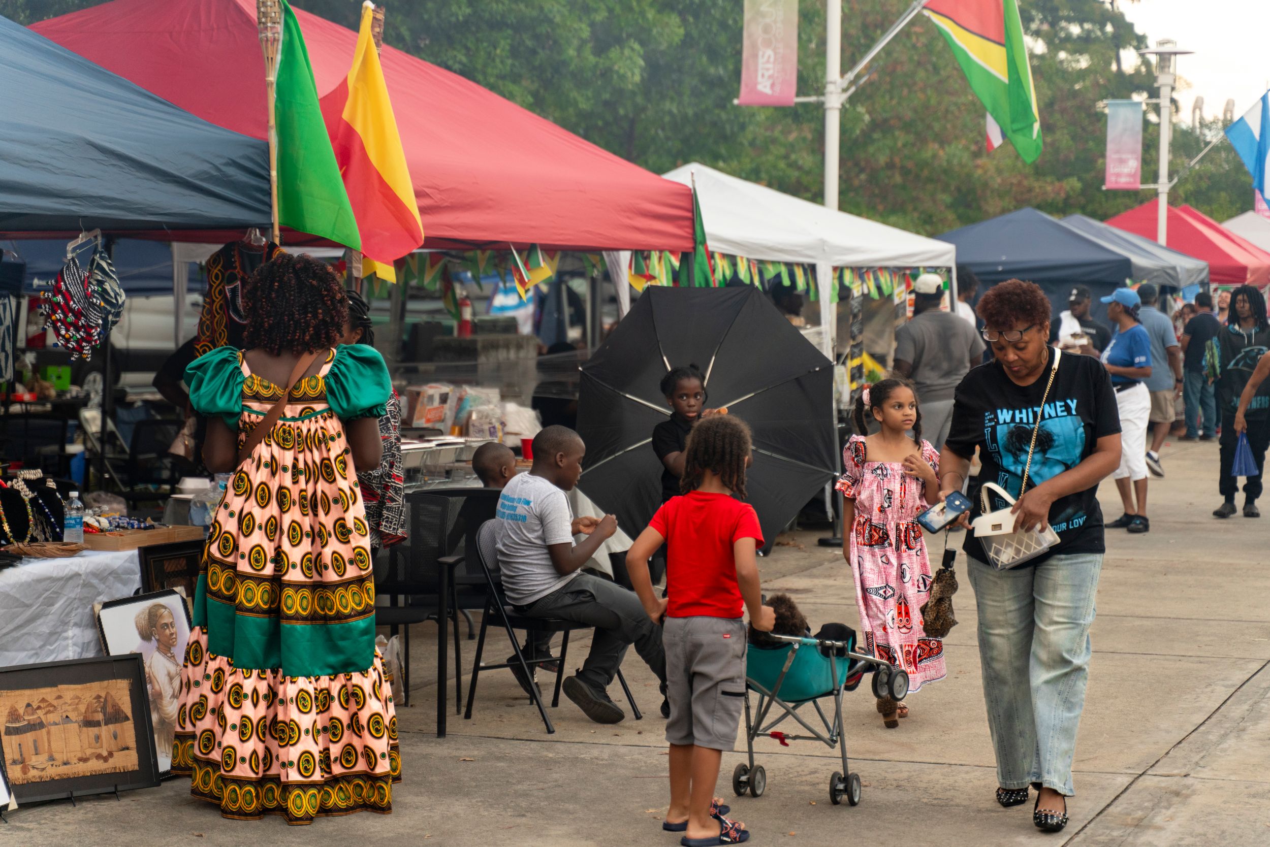 Colorful vendor tents and flags line a festival marketplace where attendees shop and browse displays.