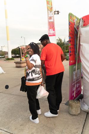 People in casual attire standing near vendor tents and flags at an outdoor festival.
