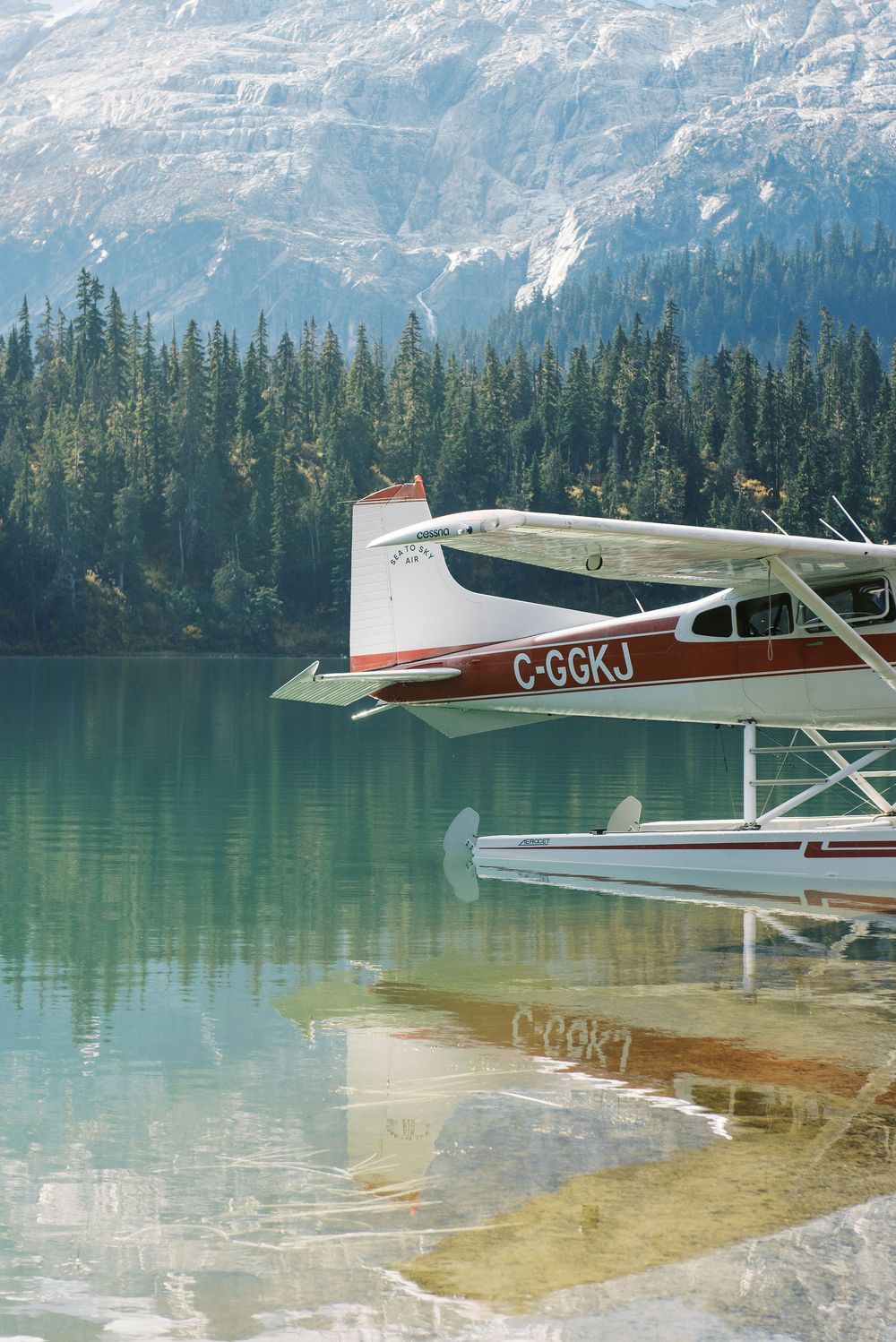 Seaplane parked on crystal clear mountain lake with snow-capped peaks in background.