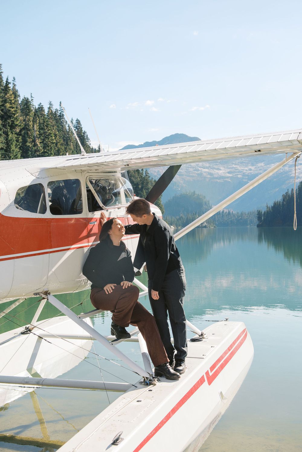 Group gathered around red and white seaplane floating on pristine mountain lake.