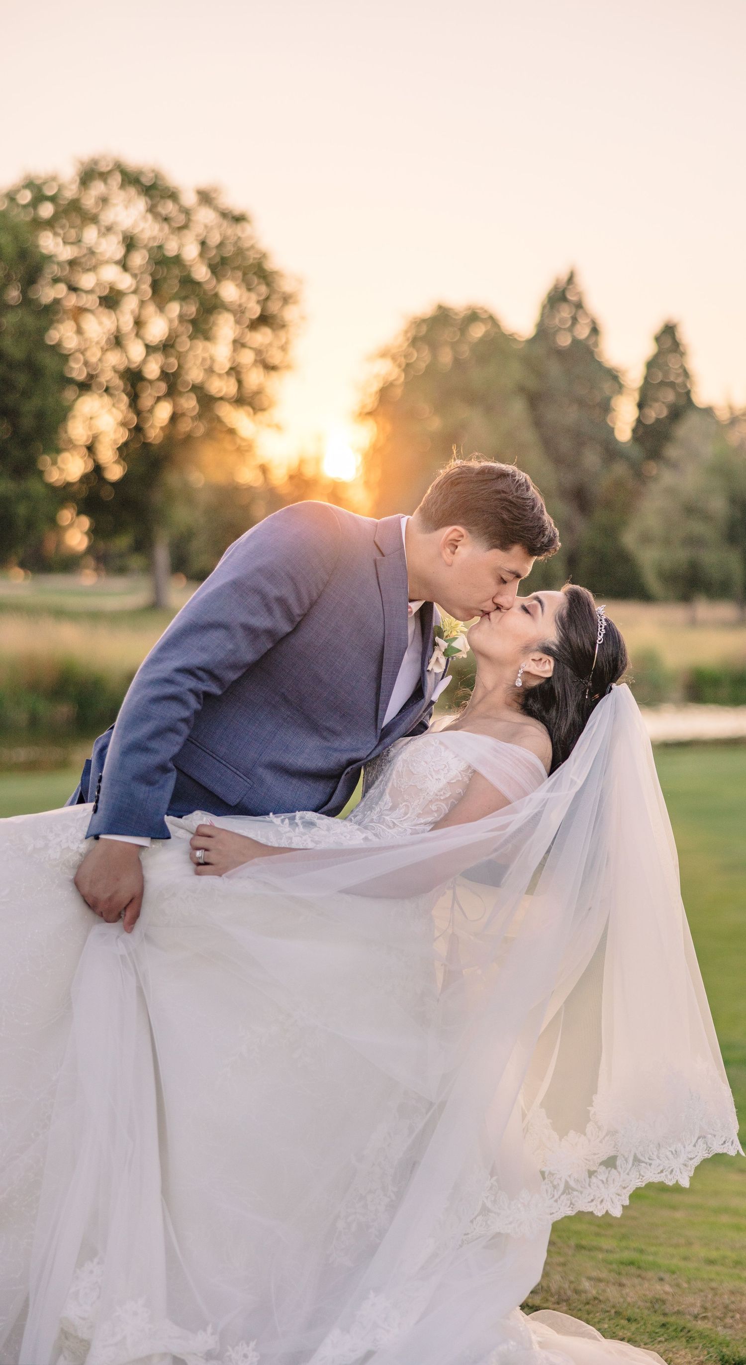 Romantic wedding couple embracing in a golden sunset on a grassy field.