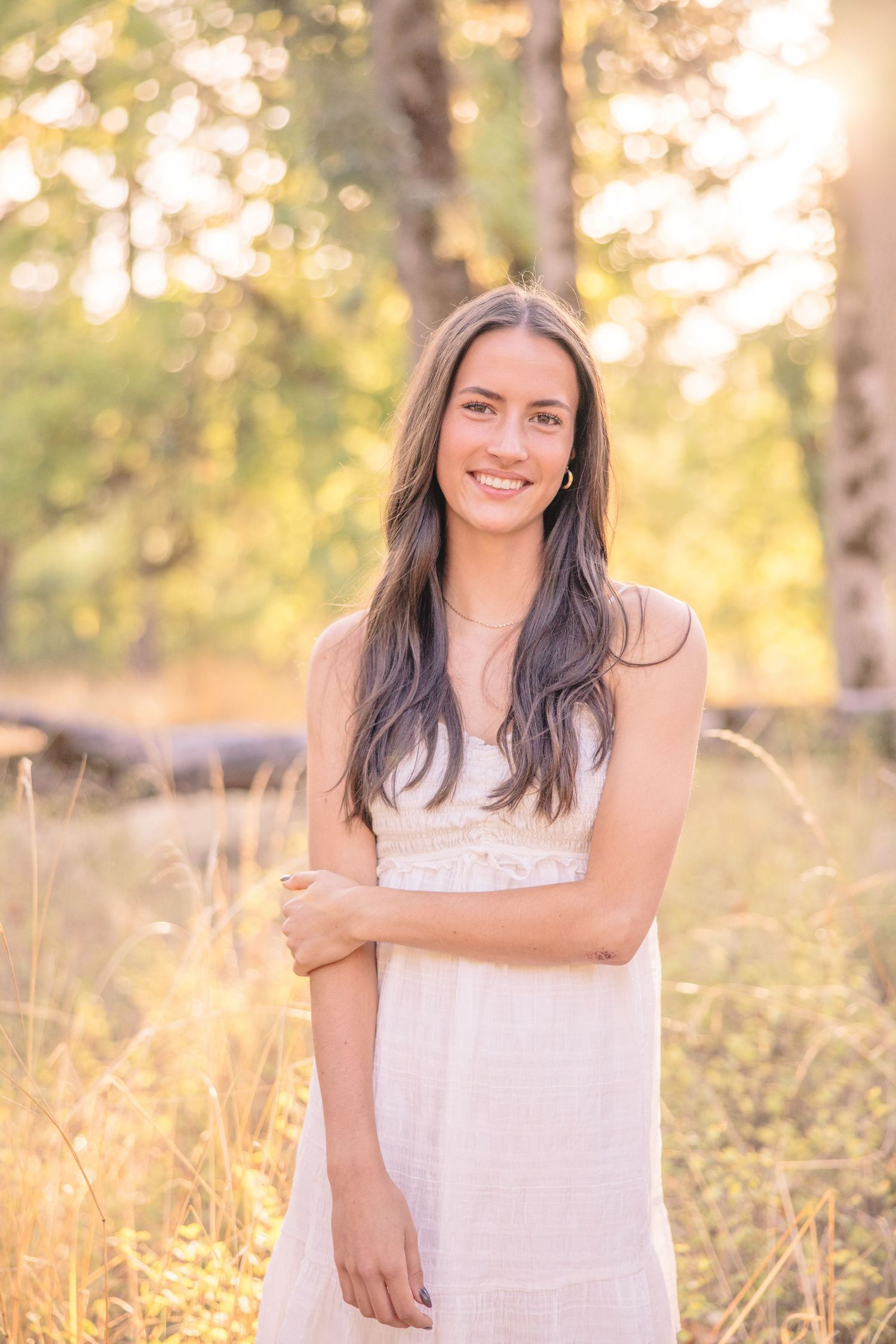 Woman in white dress poses in golden sunlit field during sunset photoshoot.