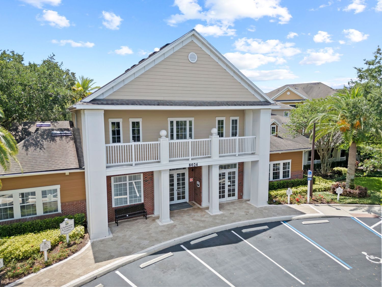 A two-story light gray office building with white columns and a front porch features parking spaces in front.