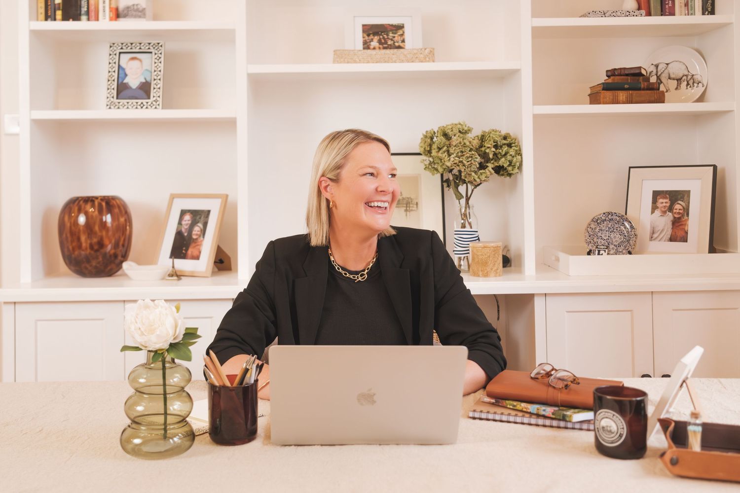 Professional woman laughing at desk with laptop and built-in shelving behind her.