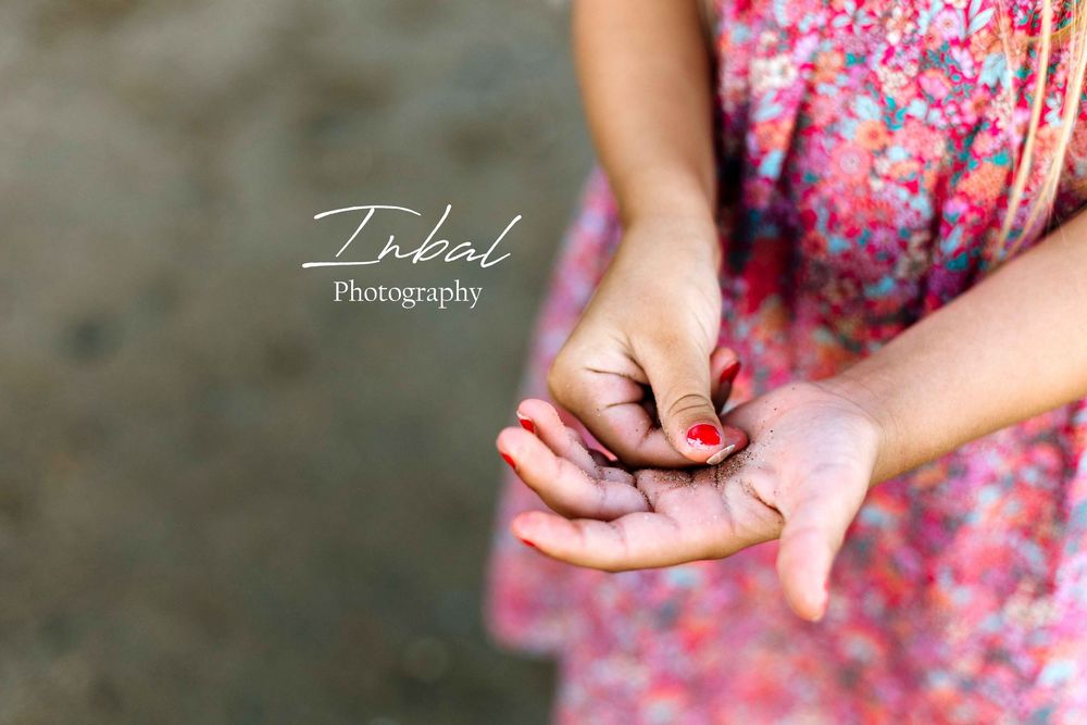 Photo of the lower half of a girl wearing a pink dress, holding a small shell in her hand while standing in the shallow sea.