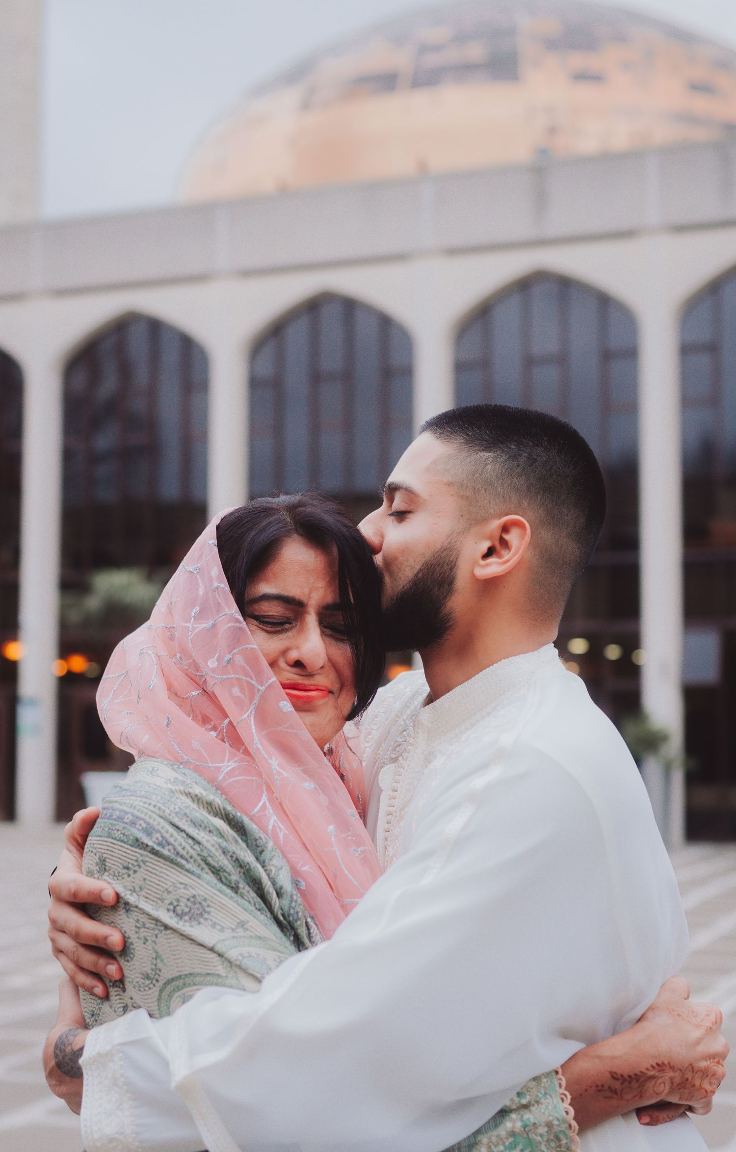 Intimate couple embraces outside a domed mosque with traditional Islamic architecture.