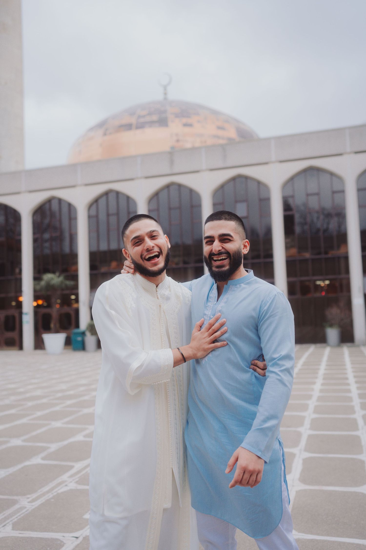 Two people in traditional white garments share joyful moment outside mosque entrance.