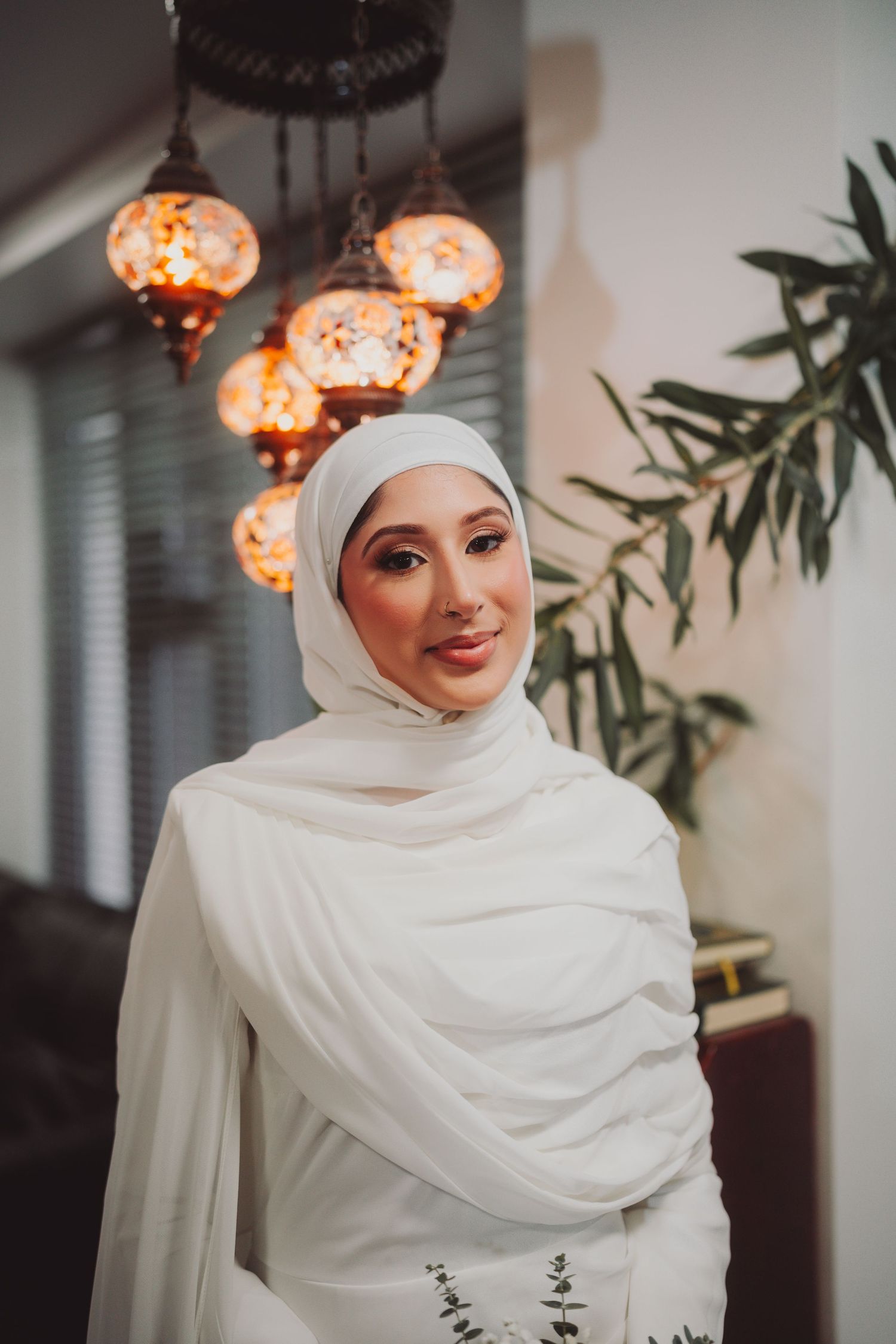 Bride in white hijab poses beneath ornate orange Moroccan lanterns.