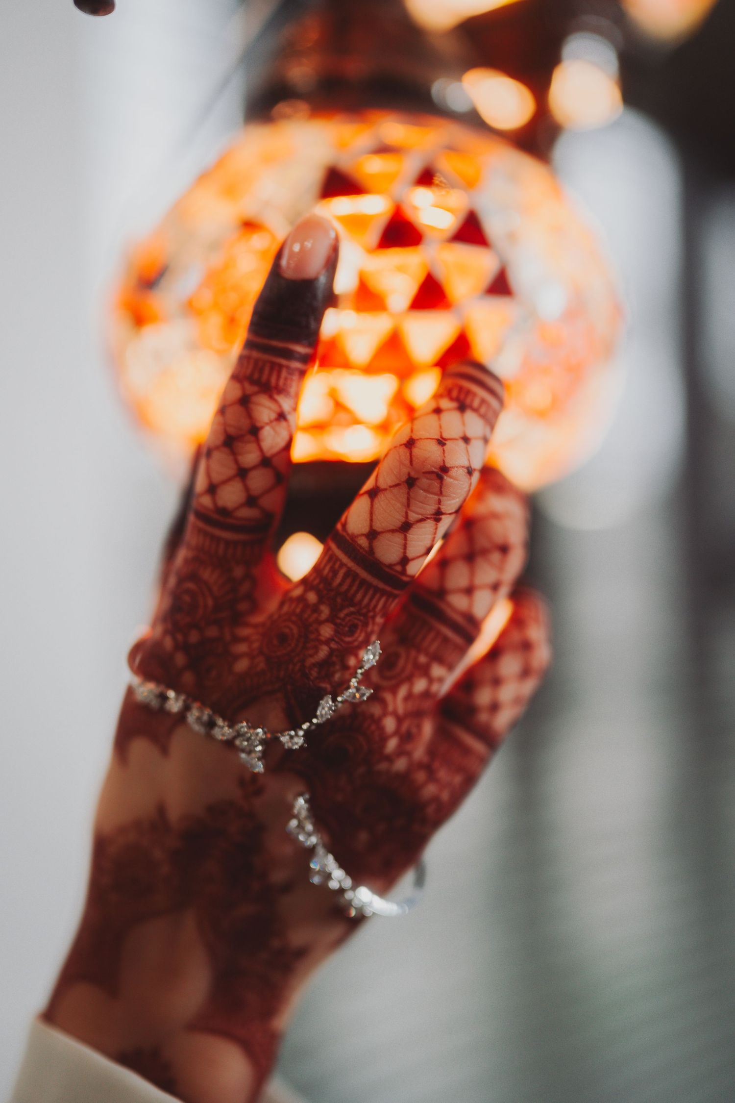 Decorated henna hand reaches toward glowing orange Moroccan lantern.