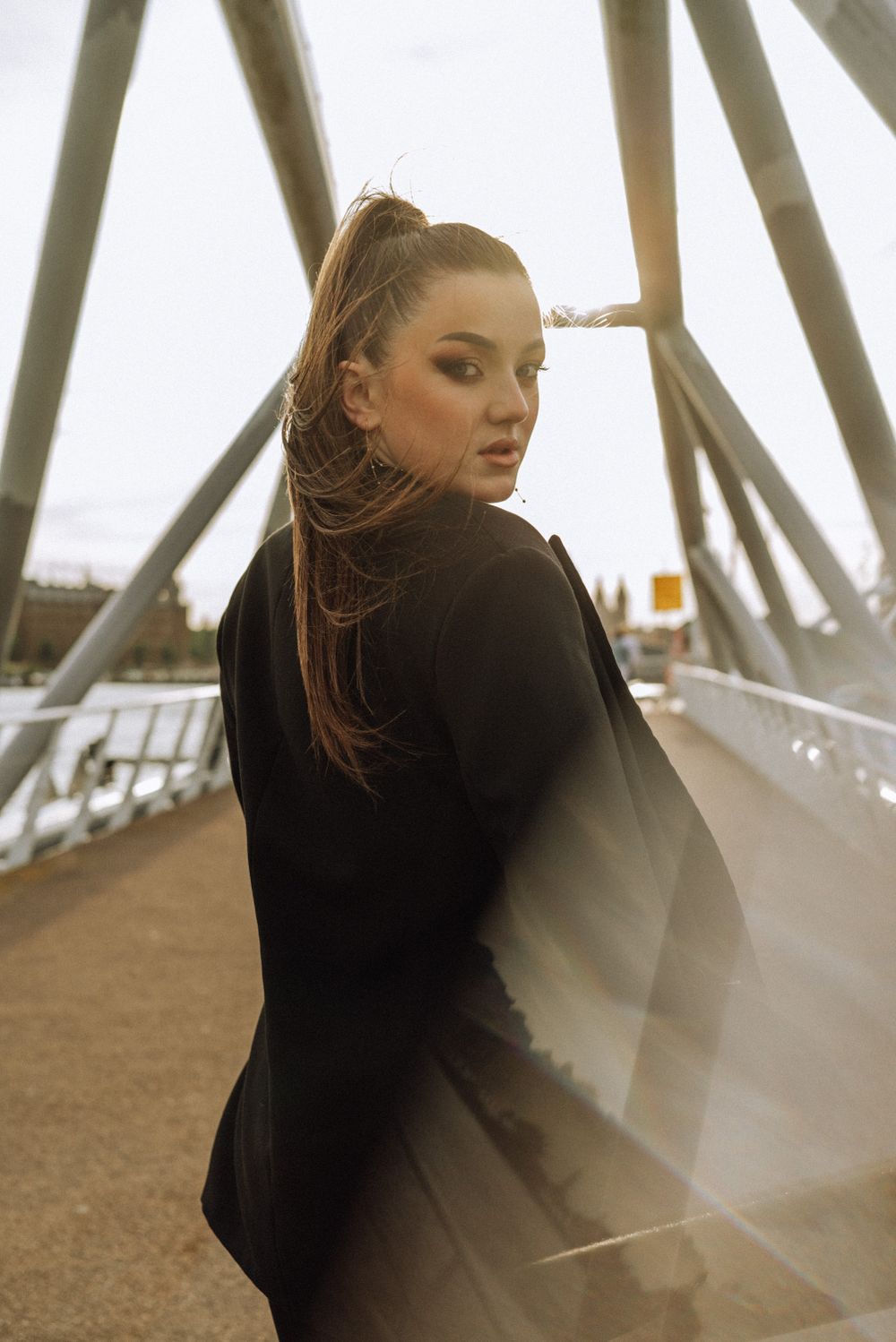 Artistic portrait against geometric metal structure in golden sunset light.
