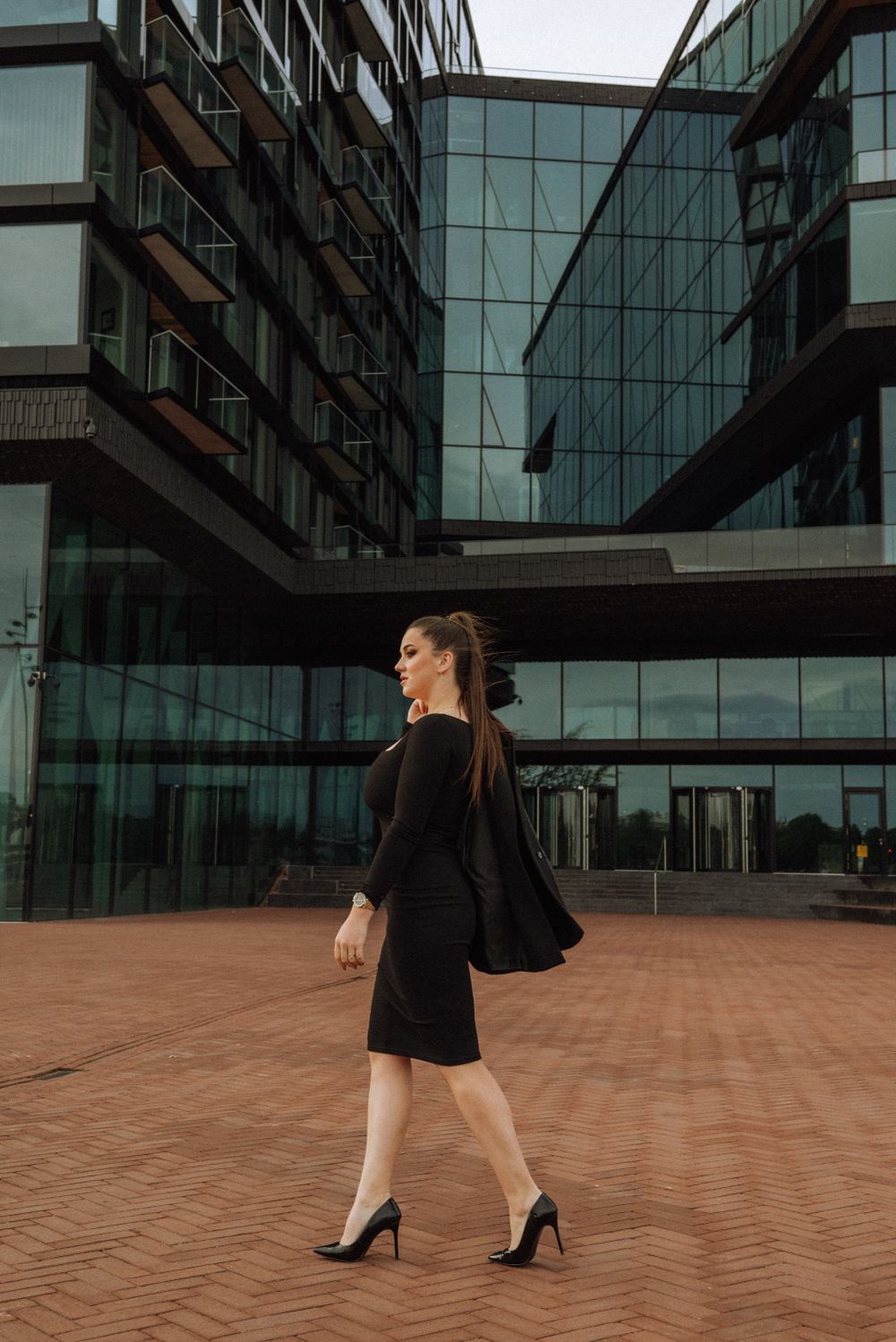 Fashion model walking across terracotta tiles near modern glass building facade.
