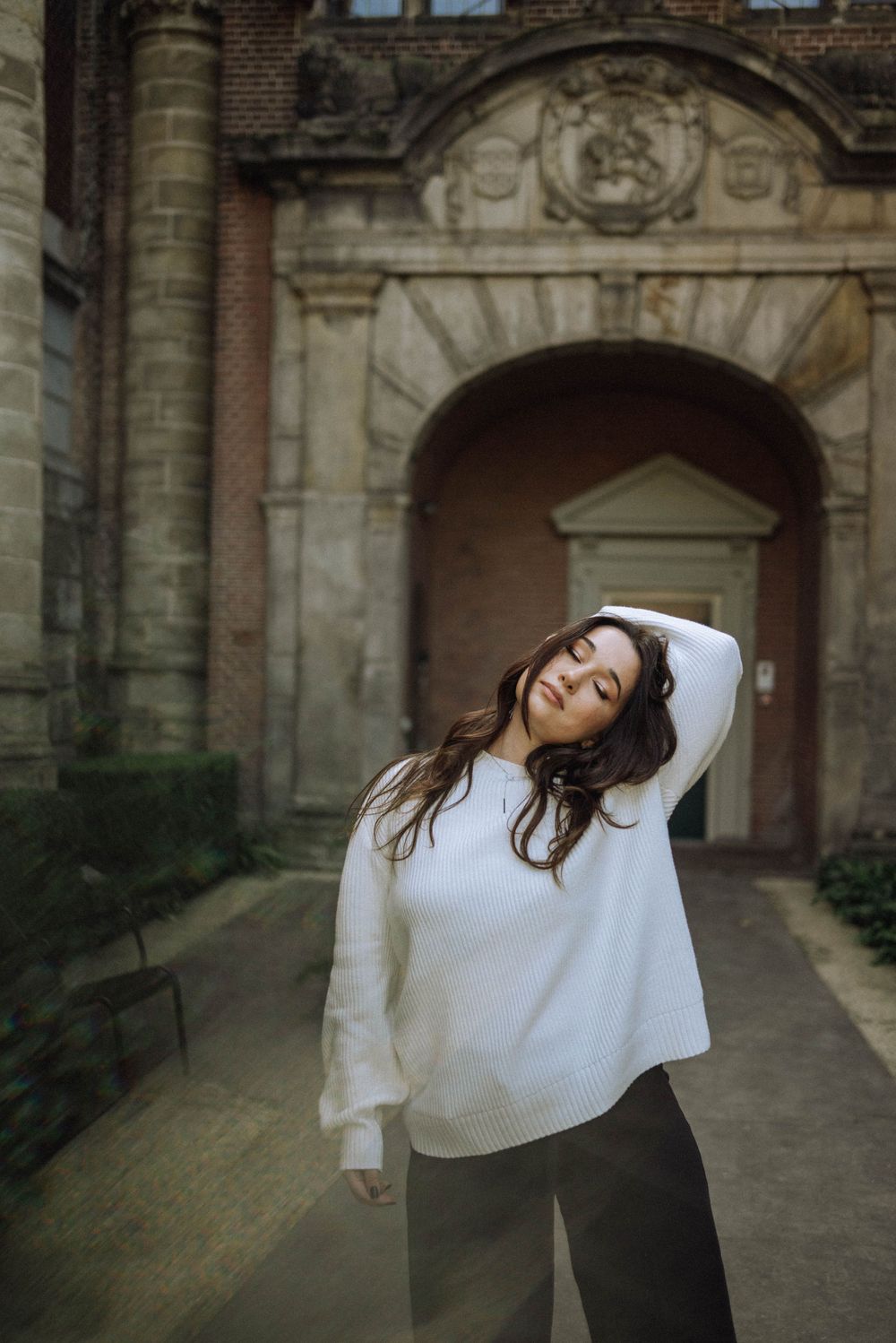 Artistic dance pose against historic stone archway and brick wall backdrop.
