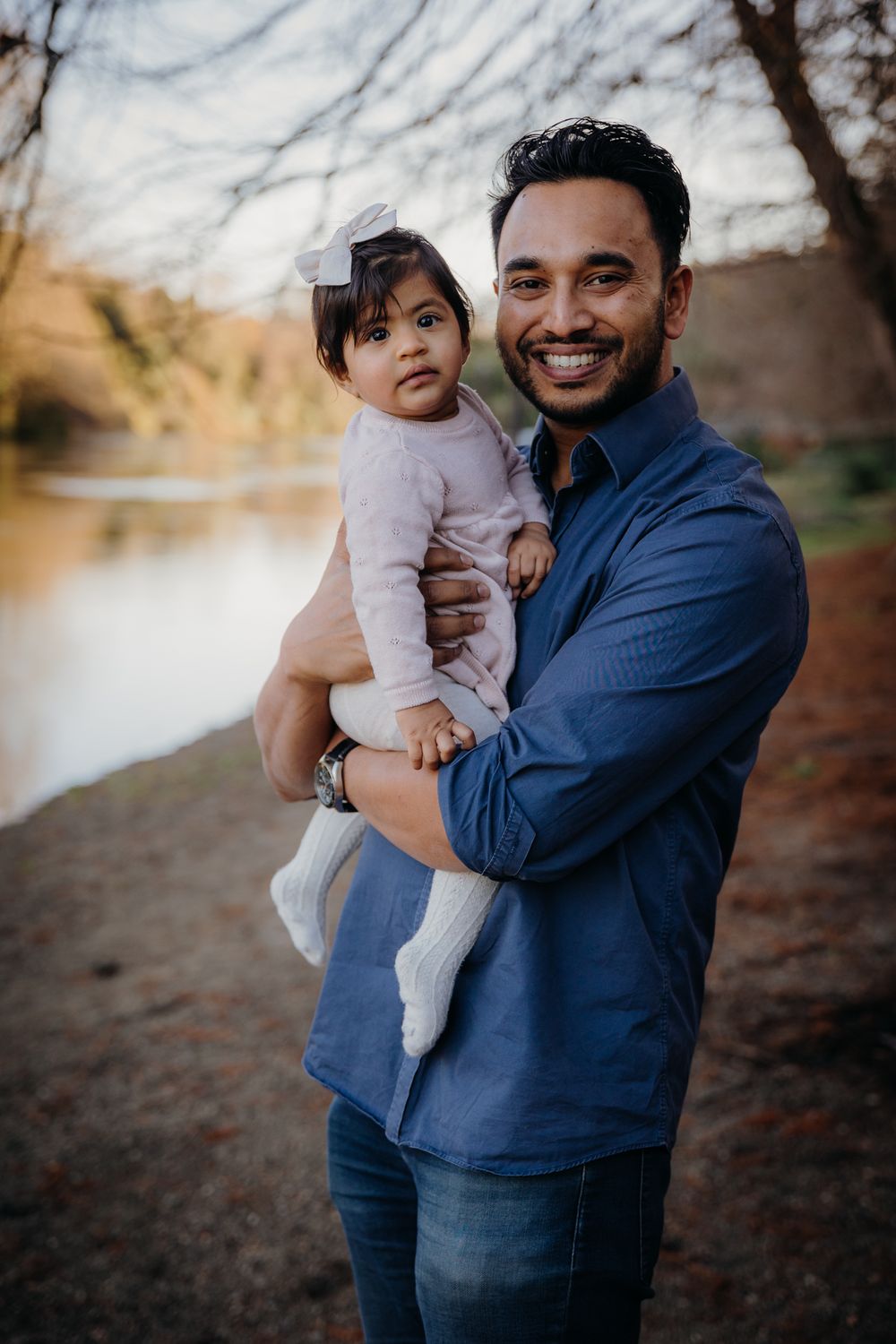 A parent and young child share a tender moment while standing near a peaceful lake on an autumn afternoon.