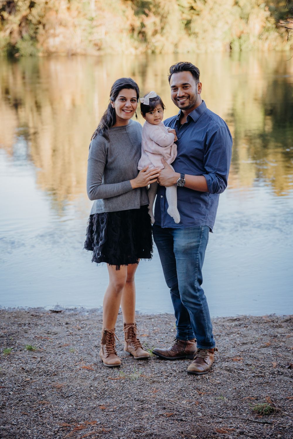 A family in casual attire poses together by a serene lake with golden reflections in the background.