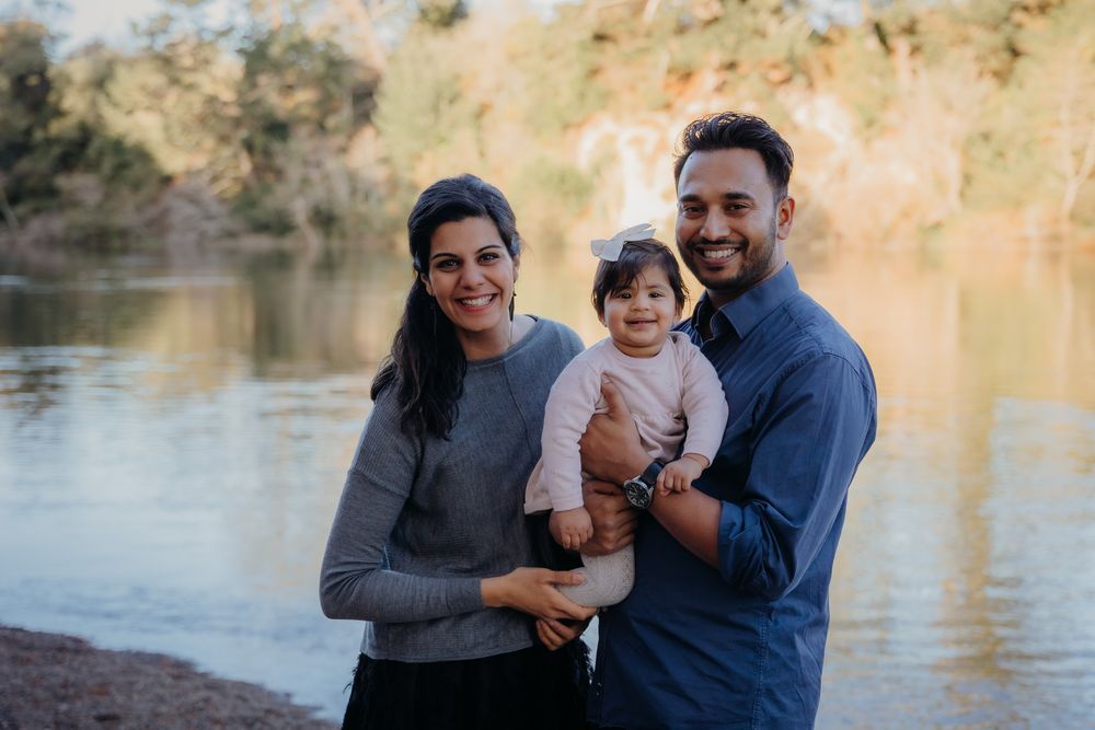Three people smiling outdoors together by a serene lakeside on a sunny afternoon.