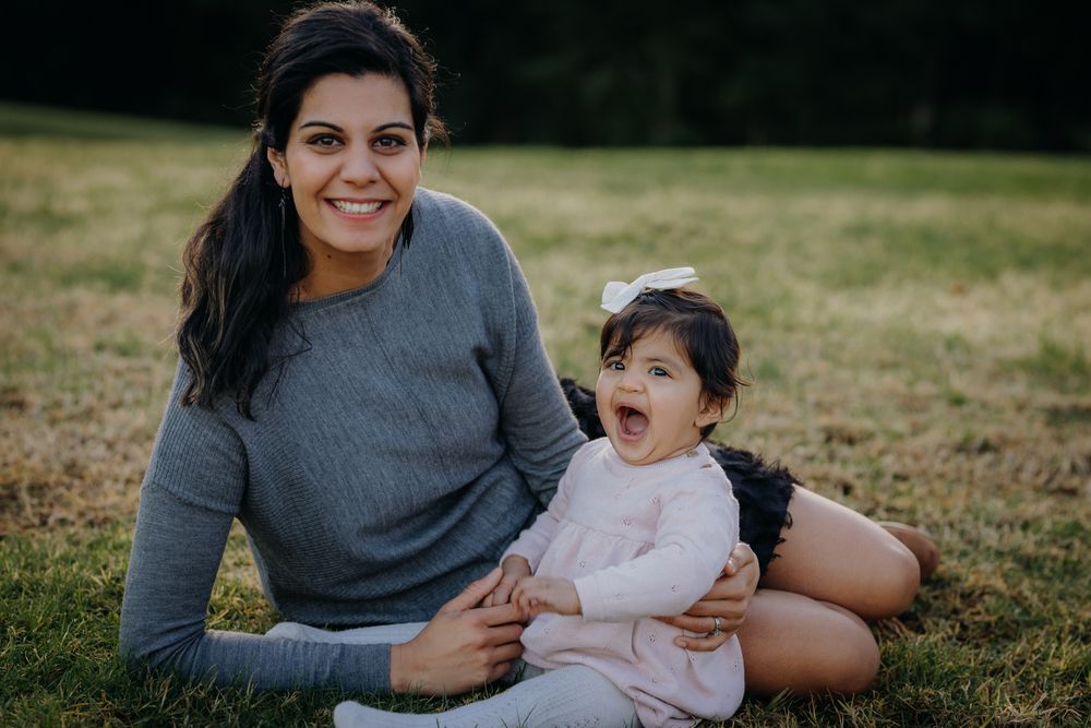 A parent and child sit together on grass outdoors, sharing a joyful moment with big smiles.